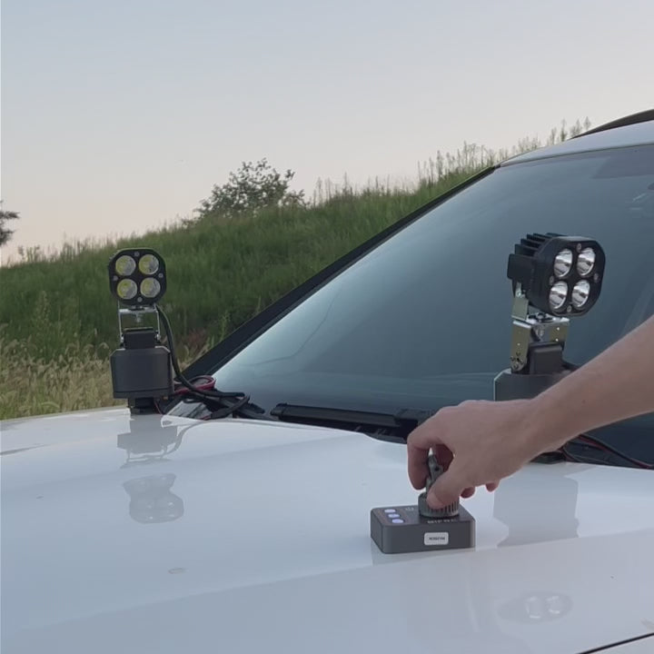 Two TRACKR360 Nightwatch S3X platforms with spotlights on a vehicle bonnet, aimed with the handheld remote